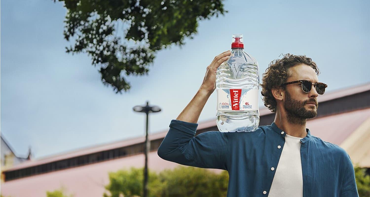  Homme tenant une grande bouteille Vittel.
